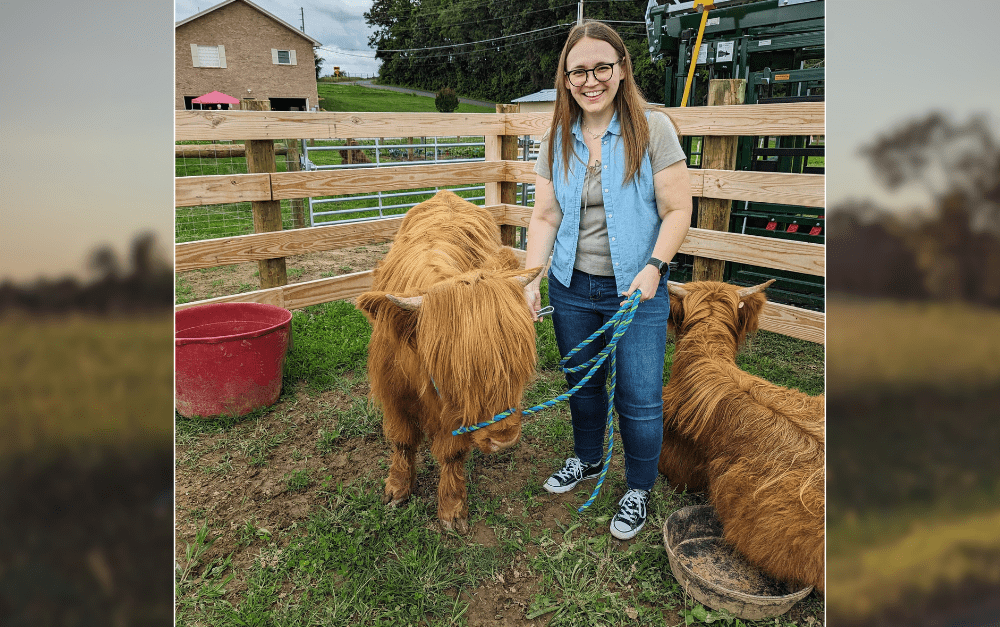 image of a smiling woman holding a leashed young highland cow.